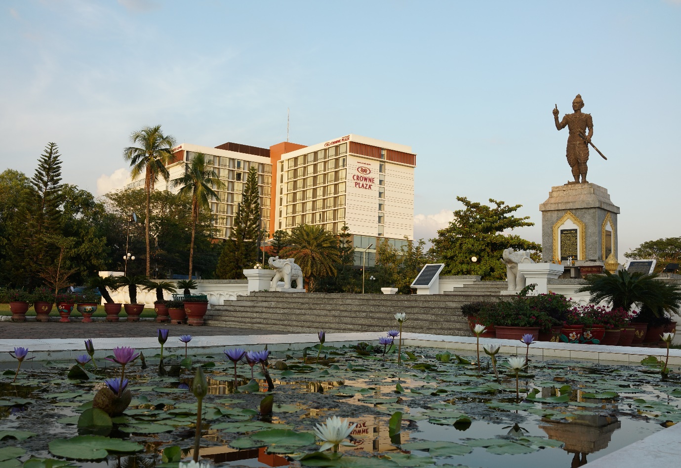 A statue of a person in a park with lily pads in front of a building

Description automatically generated